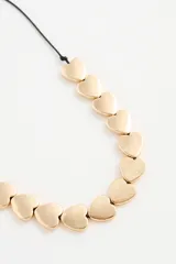 Collar dorado con dijes en forma de corazón, unidos por una cadena fina y un cordón negro.