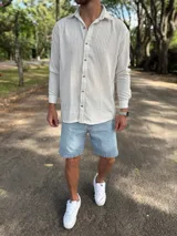 Camisa de lino blanca con rayas verticales beige, de manga larga, cuello camisero y cierre frontal de botones.