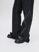 Pantalón de denim tiro alto con corte oxford y aberturas laterales en el bajo. Presenta apliques metalizados decorativos en los bolsillos delanteros y a lo largo de las costuras laterales.