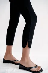 Pantalón capri negro de tiro medio con cintura elástica y detalle de alamares en el bajo.
