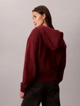 Campera canguro Calvin Klein de felpa color bordó, con capucha ajustable por cordones, cierre frontal completo de cremallera, mangas largas y bolsillos laterales. Presenta el logo monograma de la marca bordado en el pecho.