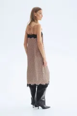 Vestido midi de satén color beige con estampado de lunares negros, breteles finos ajustables, escote recto con ribete de encaje negro, tajo lateral con detalle de encaje y bajo con terminación de encaje.