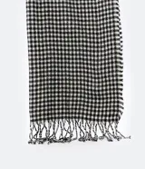 Bufanda larga de lana acrílica con estampado de cuadros blancos y negros, y flecos en los extremos.