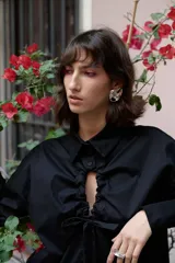 Camisa oversize de manga larga en color blanco, confeccionada en algodón. Presenta cuello clásico, puños abotonados y una abertura central ovalada con jaretas ajustables que permiten fruncir la prenda.