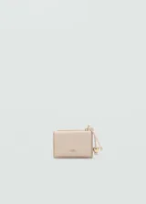 Monedero compacto de efecto piel en color beige, con cierre de solapa magnética y bolsillo lateral con cremallera. Incluye un detalle decorativo de cordón con abalorios metálicos y el logo de la marca grabado en el frente.