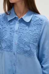 Camisa de manga larga color celeste, con cuello camisero y cierre frontal de botones. Presenta un diseño distintivo con paneles de encaje tipo crochet en la parte superior delantera.