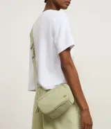 Bolso bandolera de estilo deportivo en color verde claro, confeccionado en poliéster. Cuenta con cierre principal de cremallera, bolsillo frontal con cierre, bolsillo trasero con cierre a presión, asa larga desmontable y regulable, y logo de la marca en relieve en la parte frontal.