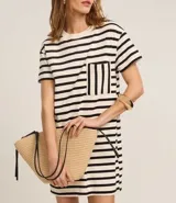 Vestido corto estilo camiseta de algodón, con cuello redondo, mangas cortas y bolsillo en el pecho. Presenta un patrón de rayas horizontales blancas y negras.