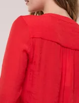 Blusa de calce relajado color salmón, confeccionada en tela liviana con textura sutil. Presenta escote en V con abotonadura frontal, bolsillo parche en el pecho, mangas largas regulables con presilla y ruedo con opción de anudar en el frente.