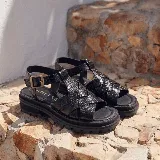 Sandalias de cuero vacuno negro con textura símil cocodrilo, diseño de tiras cruzadas, suela track de goma y hebilla metálica de ajuste en el tobillo.