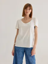 Remera de algodón con escote en V, mangas cortas con frunces en los hombros y detalle de bolsillo frontal con costuras a la vista.