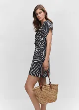 Vestido corto de estilo camisero con estampado geométrico en blanco y negro. Presenta cuello camisero, manga corta y un detalle de nudo en la cintura que aporta un diseño recto y fluido.