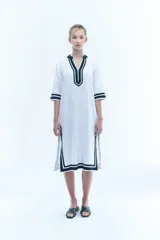 Túnica blanca de corte recto con cuello en V y mangas 3/4. Presenta detalles de ribete negro en cuello, mangas y ruedo.