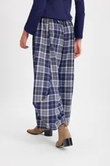 Pantalón de corte holgado con silueta tipo balloon, confeccionado en tela a cuadros. Presenta cintura elástica con cordón ajustable y cortes laterales circulares que aportan volumen a la prenda.