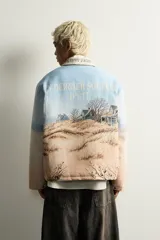Cazadora relaxed fit de tejido jacquard ligeramente acolchado, con estampado de paisaje costero y texto "Un dernier souffle d'été". Cuenta con cuello solapa con inscripción, manga larga, bolsillos de vivo en la cadera y cierre frontal con cremallera.