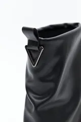 Bota de caña baja color negro, confeccionada en poliuretano con acabado liso y estructura flexible que genera un efecto fruncido. Presenta puntera redondeada, base baja y un cierre metálico en la parte trasera de la caña.