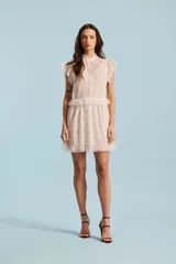 Vestido corto de encaje color crudo, con cuello alto, mangas cortas con volados, botones frontales decorativos y falda con volados en la cintura y el ruedo.