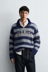 Polo de punto cepillado con diseño de rayas horizontales en azul marino y gris. Presenta cuello solapa con abertura frontal, manga larga y texto bordado en el pecho. Acabados en rib en puños y ruedo.