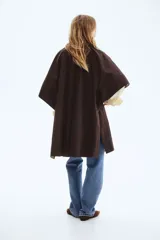 Abrigo oversized de sarga color marrón con cuello de cuero sintético. Modelo con botones en el frente, bolsillos laterales discretos, mangas tipo capa y aberturas laterales con botón.
