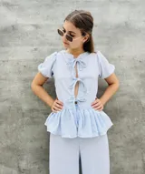 Blusa estampada con hojas verdes y blancas, con escote en V y mangas cortas abullonadas. Presenta volados en el ruedo y detalle de lazos en el frente.