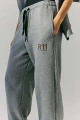 Pantalón de jogging gris de frisa con elástico ancho en cintura y puños, cordón plano ajustable, logo R11 serigrafiado y bolsillos laterales.