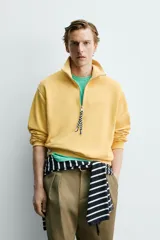 Sudadera de corte relajado confeccionada en algodón con interior de rizo, color amarillo mostaza con efecto lavado. Presenta cuello subido con cierre frontal de cremallera y detalle de cinta trenzada en el tirador, manga larga y acabados en rib.