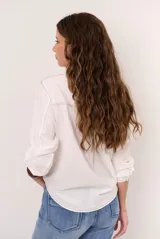 Camisa de manga larga color blanco, con cuello clásico, cierre frontal con botones marrones y costuras pespunteadas en contraste.