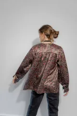 Camisa de seda con estampado floral en tonos bordó, marrón y negro. Presenta un corte amplio, escote en V con cierre frontal de botones, mangas largas abullonadas y detalles de frunce en hombros y espalda.