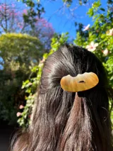 Goma de pelo con elegante pieza decorativa de nácar de forma ovalada, diseñada para aportar un toque sofisticado y único al peinado.