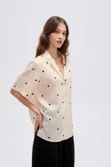 Camisa de lyocell color beige con estampado de lunares negros, cuello solapa, manga corta y cierre frontal con botones.