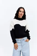 Buzo de punto con diseño bicolor en bloques ondulados de color blanco y negro. Presenta cuello alto, manga larga y una estructura de tejido marcada con calce relajado.