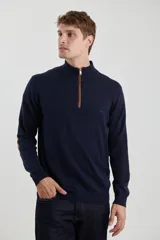 Sweater de punto gris con medio cierre frontal, cuello alto y coderas en tono marrón. Presenta un diseño clásico con puños y ruedo acanalados.