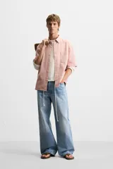Camisa de corte relajado confeccionada en algodón, con estampado de cuadros pequeños en tonos rosados. Presenta cuello solapa, manga corta y bolsillo plastrón en el pecho con cierre frontal de botones.