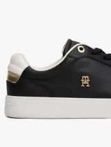 Zapatillas de corte bajo estilo tenis, confeccionadas en piel color negro. Presentan suela de goma blanca, detalle metalizado en el talón, ojal superior dorado y monograma TH metálico en el lateral.