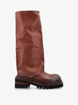 Bota de caña alta confeccionada en cuero premium color marrón, con diseño de silueta relajada y efecto arrugado. Posee suela track de goma con plataforma y taco bajo cuadrado.
