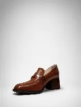 Mocasín de cuero marrón con tacón ancho efecto madera, puntera cuadrada y tira lateral con hebilla metálica y detalle texturizado.