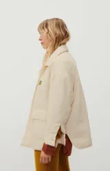 Chaqueta capitoneada color crema, de corte oversize, con cuello camisero, cierre frontal con botones a presión, bolsillos de parche y puños con abertura.