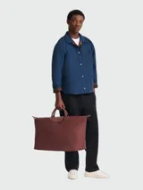 Bolso de viaje de gran tamaño, modelo Le Pliage One de Longchamp, en color marrón. Presenta el diseño icónico de la marca con solapa de cuero, asas cortas y cierre de cremallera superior.