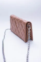 Cartera de cuero color marrón claro, con diseño capitoneado y cadena metálica plateada removible. Tiene ranuras interiores para tarjetas y documentos, y forro textil rojo.