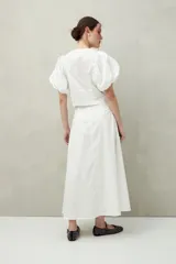 Falda larga de algodón blanca, con corte amplio y fluido, y una tabla central profunda que estiliza la figura.
