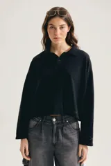 Buzo negro de algodón, con cuello polo y cierre frontal de botones, manga larga y calce oversized cropped. Presenta pequeño estampado tono sobre tono en el ruedo.