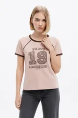 Remera de algodón color rosado, de manga corta y cuello redondo base, con ribetes marrones en contraste y estampado frontal con la inscripción "Paris 19 Legends Club".