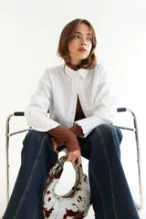 Camisa de corte boxy en color blanco, con cuello clásico, cierre frontal de botones y mangas largas con puños estructurados con tablas. Presenta costuras a contratono y detalle de frunce en la espalda.