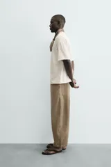 Jeans de hombre, tiro medio, color marrón claro o caqui, con corte relaxed fit y perneras anchas. Presenta cinco bolsillos y costuras laterales giradas hacia el frente.
