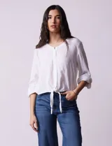 Blusa blanca de algodón marca Dash, con escote en V, abertura con botones, mangas 3/4 regulables con presilla y botón, y terminación de ruedo anudado.