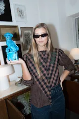 Blusa de algodón con estampado a cuadros en tonos marrón y negro. Presenta un diseño de corte asimétrico en el frente, mangas largas levemente abullonadas y detalles de bordados florales en la zona del canesú.