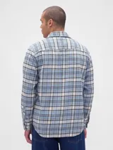 Camisa de manga larga confeccionada en tela de franela con estampado de cuadros en tonos azul claro, blanco y negro. Presenta cuello clásico, cierre frontal con botones y un bolsillo en el pecho.