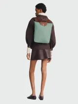 Mochila de diseño minimalista en color beige, con solapa y asa superior en cuero marrón texturizado. Cuenta con correas ajustables en color marrón y cierre principal.
