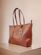 Bolso tote grande de cuero color marrón con textura tipo reptil. Tiene doble asa de hombro, cierre superior y bolsillo frontal con cierre. Incluye un dije colgante en forma de estrella con flecos plateados.