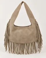 Cartera estilo hobo de gamuza color beige, con flecos largos colgantes en los laterales y la base. Cuenta con asa ancha integrada y cierre superior con cremallera.